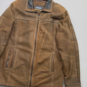 Pu&ograve; includere: Una giacca in pelle marrone con colletto nero e cerniere nere. La giacca presenta una chiusura centrale con zip, due tasche verticali con zip sul davanti e un'etichetta all'interno del colletto con la scritta SWEEP Young Fashion.