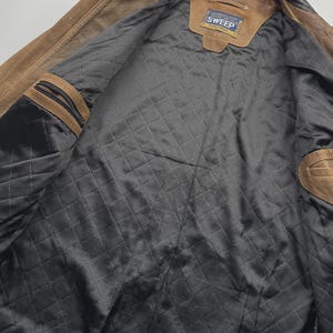 Pu&ograve; includere: Una giacca in pelle color cuoio con fodera interna nera trapuntata. La giacca presenta un colletto nero, due tasche interne sul petto con chiusura a zip e un'etichetta rettangolare sul collo con la scritta Continental Wear For Long Time Use SWEEP.
