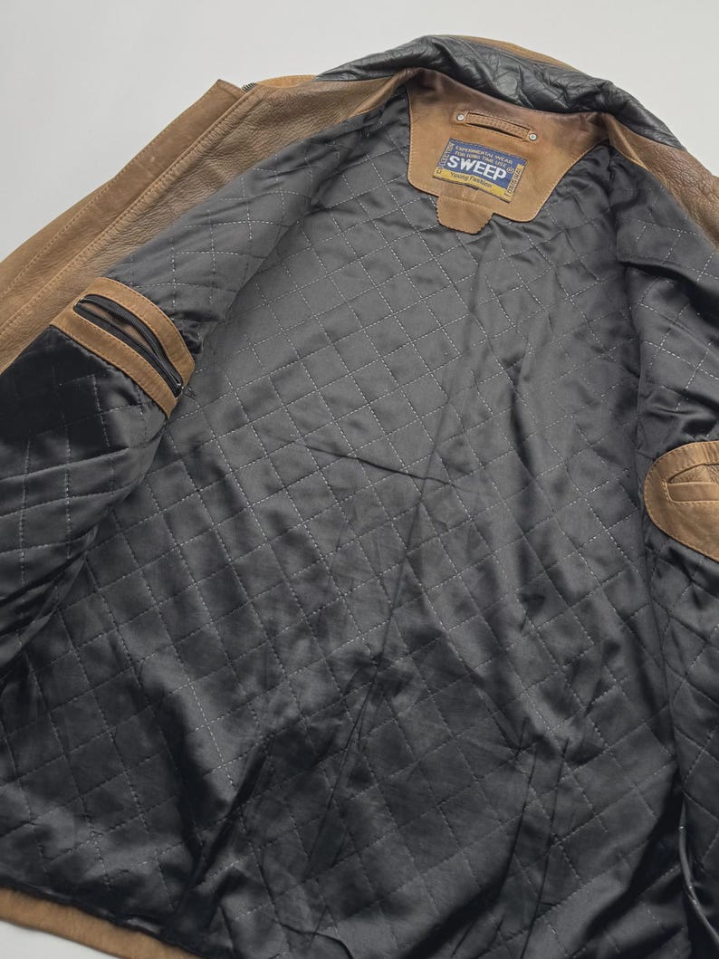 Pu&ograve; includere: Una giacca in pelle color cuoio con fodera interna nera trapuntata. La giacca presenta un colletto nero, due tasche interne sul petto con chiusura a zip e un'etichetta rettangolare sul collo con la scritta Continental Wear For Long Time Use SWEEP.