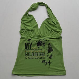 Può includere: Un top all'americana color verde lime con una stampa grafica nera che riporta il testo MY LOVES CODE EACH GIRL IS FULL OF THE ENERGY In former days glory. Il design include piccoli accenti a forma di stella dorata e una silhouette.