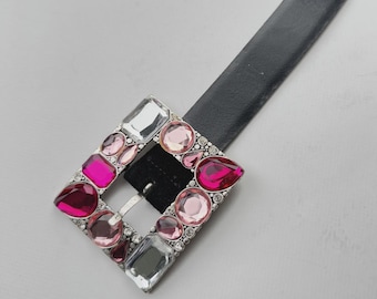 May include: A black leather belt with a square buckle adorned with pink and clear rhinestones.