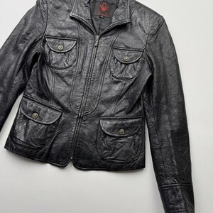 以下が含まれることがあります： ジッパー留めと複数のポケットが付いた黒い革のジャケット。ジャケットの襟の内側には、「Schiaparelli」という文字が書かれた小さな赤いラベルが付いています。