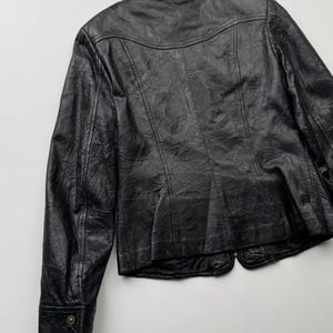 以下が含まれることがあります： ジッパー留めとスタンドカラーのブラックレザージャケット。ジャケットはテクスチャ加工が施され、少し短めの丈です。