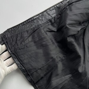 以下が含まれることがあります： 黒い革のジャケットの裏地は、滑らかで質感のある生地です。裏地は開いたジッパーから見えています。