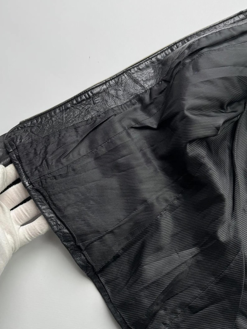 以下が含まれることがあります： 黒い革のジャケットの裏地は、滑らかで質感のある生地です。裏地は開いたジッパーから見えています。