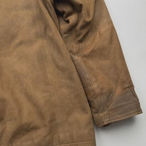 Pu&ograve; includere: Una giacca in pelle color cuoio con una finitura opaca liscia, caratterizzata da cuciture verticali visibili lungo il pannello frontale e una manica lunga con un'area del gomito rinforzata. Il capo presenta un colore marrone chiaro uniforme.
