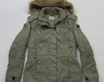 May include: An olive green parka-style jacket with a faux fur-lined hood. The jacket features multiple pockets, button closures, and quilted elbow patches. The label reads "John Baner".