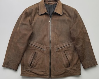 Puede incluir: Chaqueta de cuero marrón con cremallera y cuello. La chaqueta tiene dos bolsillos delanteros y un forro oscuro. El cuero tiene un aspecto envejecido.