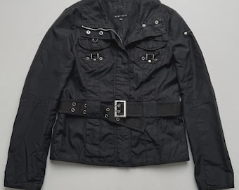 May include: A black jacket with a high collar, long sleeves, and a front zip fastening. The garment features two chest pockets with flaps, silver-tone metal hardware, and a matching black fabric belt with a rectangular silver buckle at the waist.