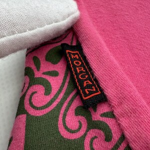 May include: Close-up of a pink and green patterned fabric with a black tag that says "MORGAN" in orange lettering.