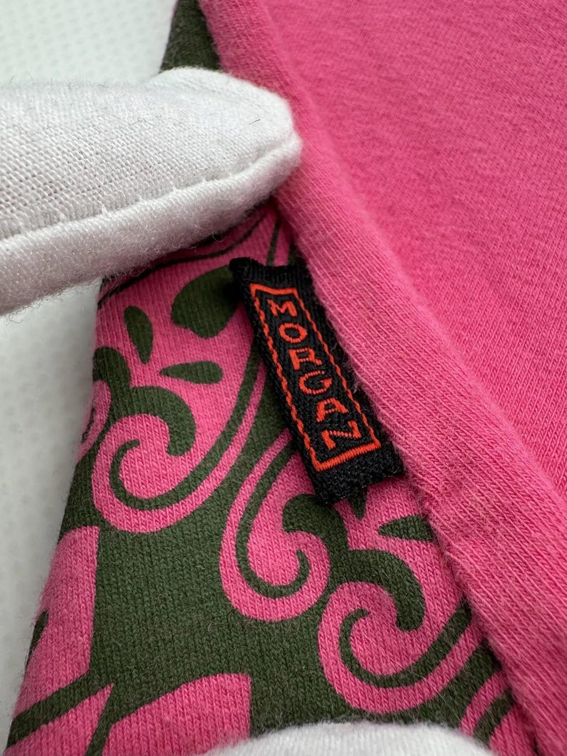 May include: Close-up of a pink and green patterned fabric with a black tag that says "MORGAN" in orange lettering.
