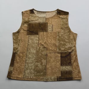 May include: A sleeveless top featuring a patchwork design in various shades of brown and tan. The garment displays rectangular panels with different textures and patterns, joined by visible decorative cross-stitch detailing throughout.