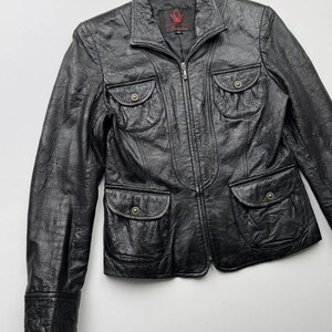 以下が含まれることがあります： ジッパー留めと複数のポケットが付いた黒い革のジャケット。ジャケットの襟の内側に「Valentino」という文字の小さなラベルが付いています。