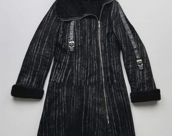 May include: Black long coat with a textured, vertical stripe pattern. The coat features a large, black, faux fur collar and cuffs. It has a diagonal zip closure and silver-tone buckles. The coat is a mid-length style.