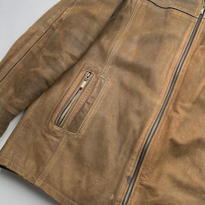 Pu&ograve; includere: Una giacca in pelle color cuoio con chiusura frontale a zip, una tasca verticale con zip sul petto e un colletto marrone scuro. La giacca presenta cuciture visibili lungo i pannelli e una finitura testurizzata e vissuta sulla pelle.