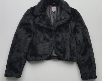May include: A black faux fur jacket with a wide collar and a single-button closure. The jacket has long sleeves and a cropped length, offering a stylish and warm outerwear option. The jacket is made of a soft, plush material.