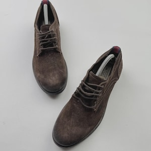 Op de afbeelding: Paar bruine su&egrave;de veterschoenen. De schoenen hebben een distressed look en een donkerbruine zool. De veters zijn bruin en de schoenen worden op een witte achtergrond gepresenteerd. De schoenen zijn nieuw en hebben schoenspanners.