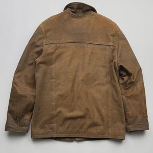 Pu&ograve; includere: Una giacca in camoscio marrone con colletto alto, maniche lunghe con polsini e una cucitura orizzontale sulla parte superiore della schiena. Il capo presenta dettagli con cuciture a vista lungo i pannelli verticali e una texture liscia e opaca.