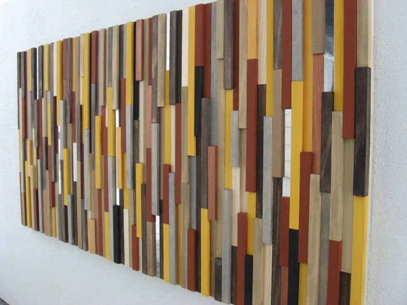 Puede incluir: Una pieza de arte de pared hecha de varias piezas de madera de diferentes colores y tama&ntilde;os. Las piezas de madera est&aacute;n dispuestas en un patr&oacute;n vertical, creando un dise&ntilde;o moderno y abstracto. Los colores incluyen tonos de marr&oacute;n, amarillo, rojo y gris.