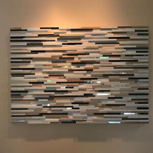 May include: A wall art piece made of wood and mirror tiles. The tiles are arranged in a horizontal pattern, creating a modern and abstract design. The piece is a light brown, white, and black color.