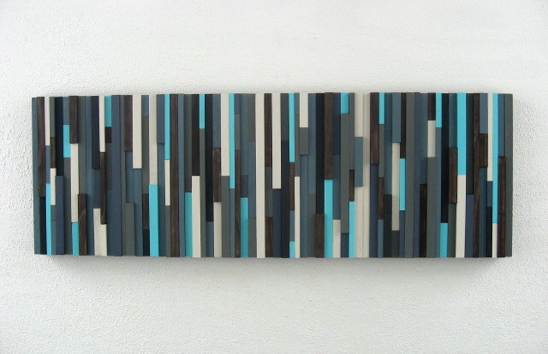 Pu&ograve; includere: Arte da parete astratto realizzato in legno con una variet&agrave; di tonalit&agrave; di blu, grigio, marrone e bianco. Il legno &egrave; disposto in strisce verticali per creare un design moderno e geometrico.