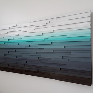 May include: Abstract wall art made of wood with a gradient of colors from white to dark gray, with a turquoise blue stripe in the middle.