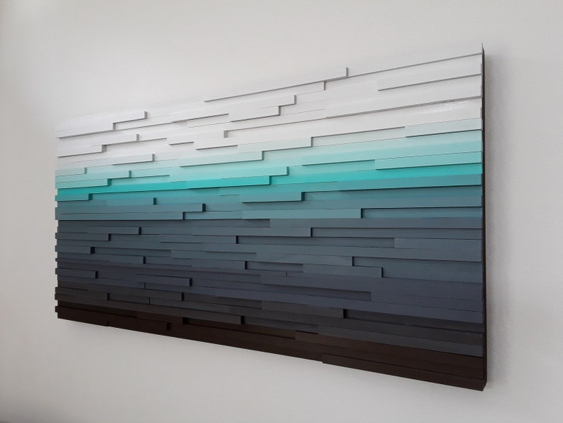 May include: Abstract wall art made of wood with a gradient of colors from white to dark gray, with a turquoise blue stripe in the middle.