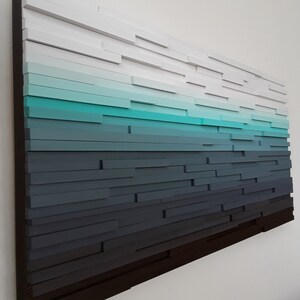 May include: A wall art piece made of wood with a gradient of colors from white to dark blue. The wood is arranged in horizontal rows, creating a layered effect.