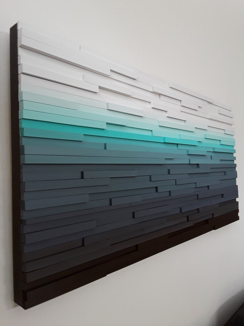May include: A wall art piece made of wood with a gradient of colors from white to dark blue. The wood is arranged in horizontal rows, creating a layered effect.