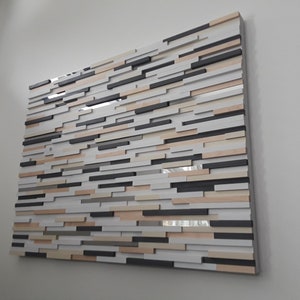 May include: A wall art piece made of wood with a layered, geometric design. The wood is painted in shades of white, gray, black, and beige.