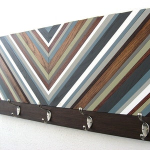 May include: A wooden wall-mounted coat rack with a chevron pattern in shades of brown, gray, and white. The rack has five metal hooks.