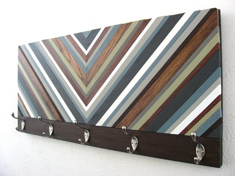 May include: A wooden wall-mounted coat rack with a chevron pattern in shades of brown, gray, and white. The rack has five metal hooks.