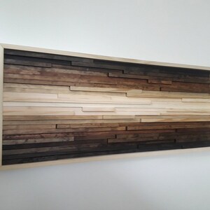 May include: A framed wood wall art piece with a gradient of brown, beige, and white wood strips arranged horizontally. The wood strips are of varying lengths and widths, creating a textured and abstract design.