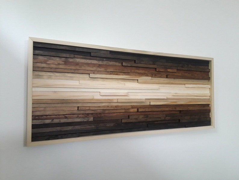 May include: A framed wood wall art piece with a gradient of brown, beige, and white wood strips arranged horizontally. The wood strips are of varying lengths and widths, creating a textured and abstract design.