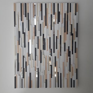 May include: A rectangular mirror with a unique design. The mirror is made up of many small, rectangular pieces of wood in various shades of brown, white, and black. The pieces are arranged in a random pattern, creating a modern and abstract look.