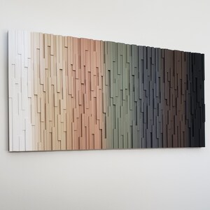 May include: A wall art piece made of wood with a gradient of colors from white to black. The wood is arranged in a vertical pattern, creating a textured look.