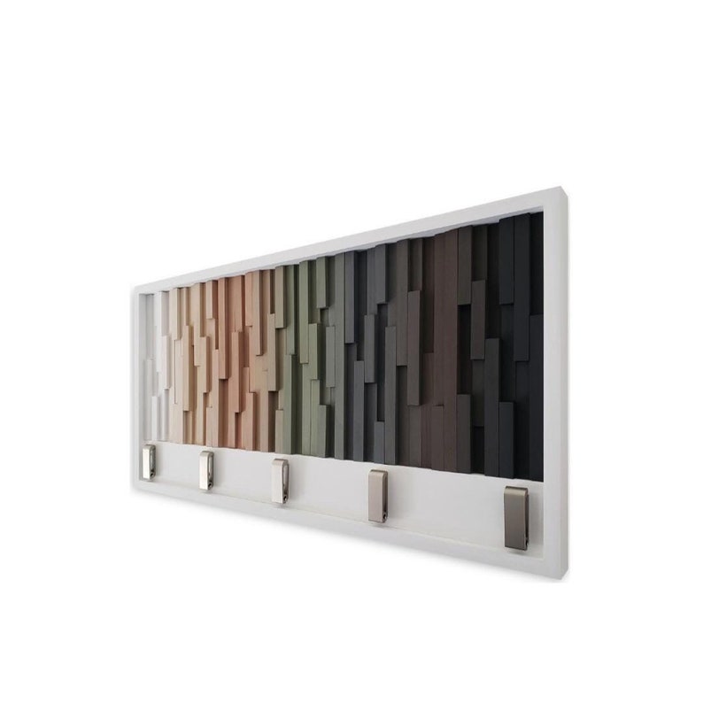 May include: White wall-mounted key holder with a geometric design of wooden blocks in shades of beige, green, and brown. The holder has five metal hooks.
