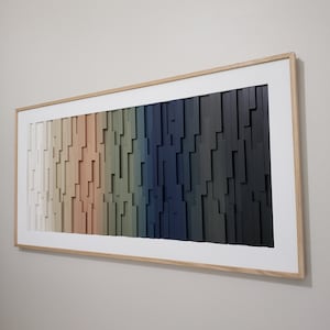 May include: A framed abstract wall art piece with a gradient of colors, starting with white and transitioning to dark blue. The art is made of wood and has a geometric pattern.