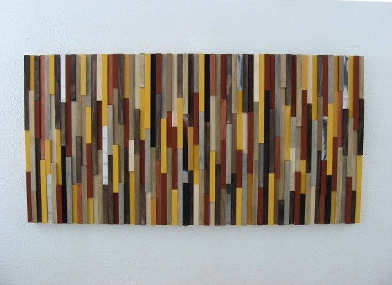 Puede incluir: Una pieza de arte de pared hecha de varias tiras de madera en tonos de marr&oacute;n, amarillo y rojo. Las tiras est&aacute;n dispuestas verticalmente y crean un dise&ntilde;o moderno y abstracto.