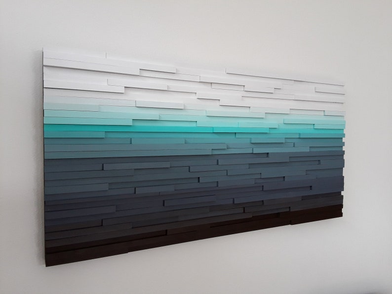 May include: Abstract wall art made of wood with a gradient of colors from white to black, with a turquoise blue band in the middle.
