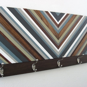 May include: A wooden wall-mounted coat rack with a chevron pattern in shades of brown, gray, and white. The rack has five silver hooks.