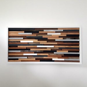 May include: A rectangular wooden wall art piece with a white frame. The art is made of various wood planks in different shades of brown, gray, and white. The planks are arranged in a horizontal pattern, creating a modern and abstract design.