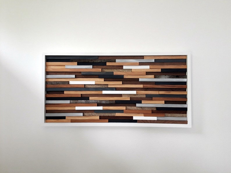 May include: A rectangular wooden wall art piece with a white frame. The art is made of various wood planks in different shades of brown, gray, and white. The planks are arranged in a horizontal pattern, creating a modern and abstract design.