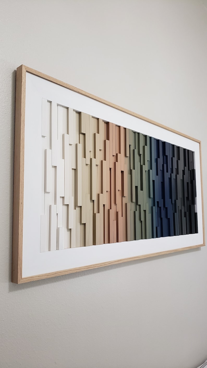 May include: A framed wood wall art piece with a gradient of colors from white to dark blue. The wood pieces are arranged in a staggered pattern, creating a textured effect.
