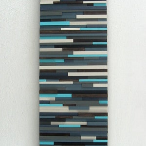 Pu&ograve; includere: Arte murale astratto realizzato con listelli di legno in tonalit&agrave; di blu, grigio e bianco. I listelli sono disposti in un motivo orizzontale, creando un design moderno e minimalista.