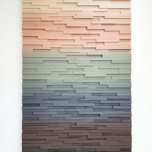 May include: A wall art piece made of wood painted in a gradient of colors, starting with white and transitioning to black. The wood is arranged in horizontal rows, creating a layered effect.