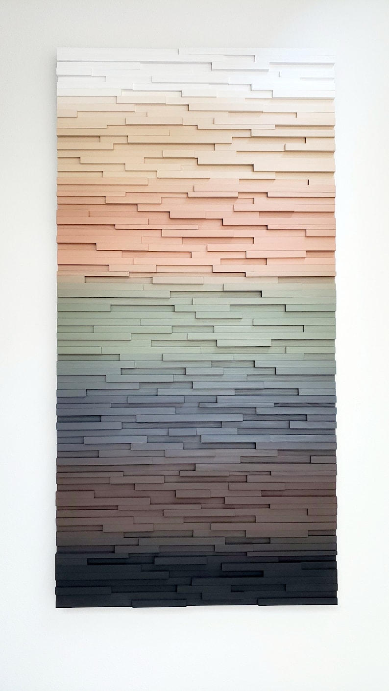 May include: A wall art piece made of wood painted in a gradient of colors, starting with white and transitioning to black. The wood is arranged in horizontal rows, creating a layered effect.
