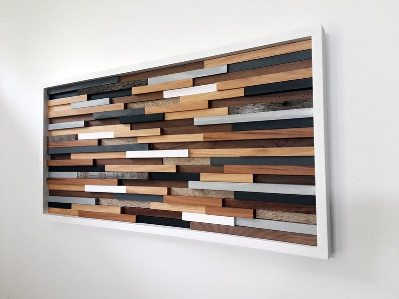May include: A framed wall art piece made of wood with a variety of colors and textures. The wood is arranged in a geometric pattern, creating a modern and abstract design. The frame is white and adds a clean and minimalist touch to the piece.