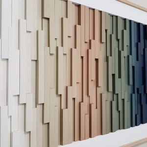 May include: A framed wall art piece made of wood with a gradient of colors from white to dark blue. The wood is arranged in a staggered pattern, creating a textured effect.