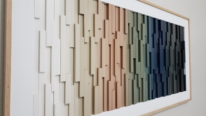 May include: A framed wall art piece made of wood with a gradient of colors from white to dark blue. The wood is arranged in a staggered pattern, creating a textured effect.